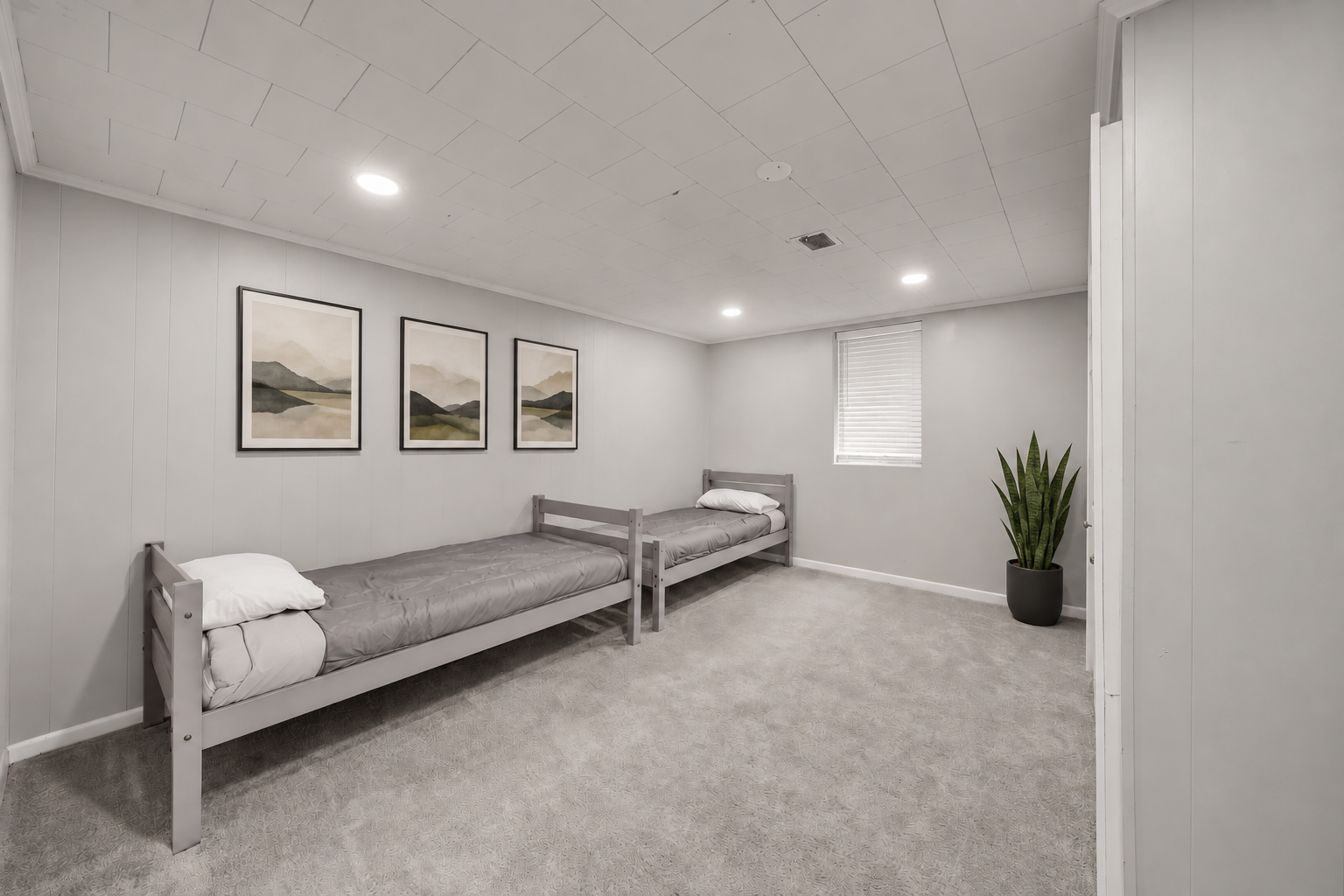 RCVRY HOUSE basement bedroom with two twin beds, framed landscape art, and plant
