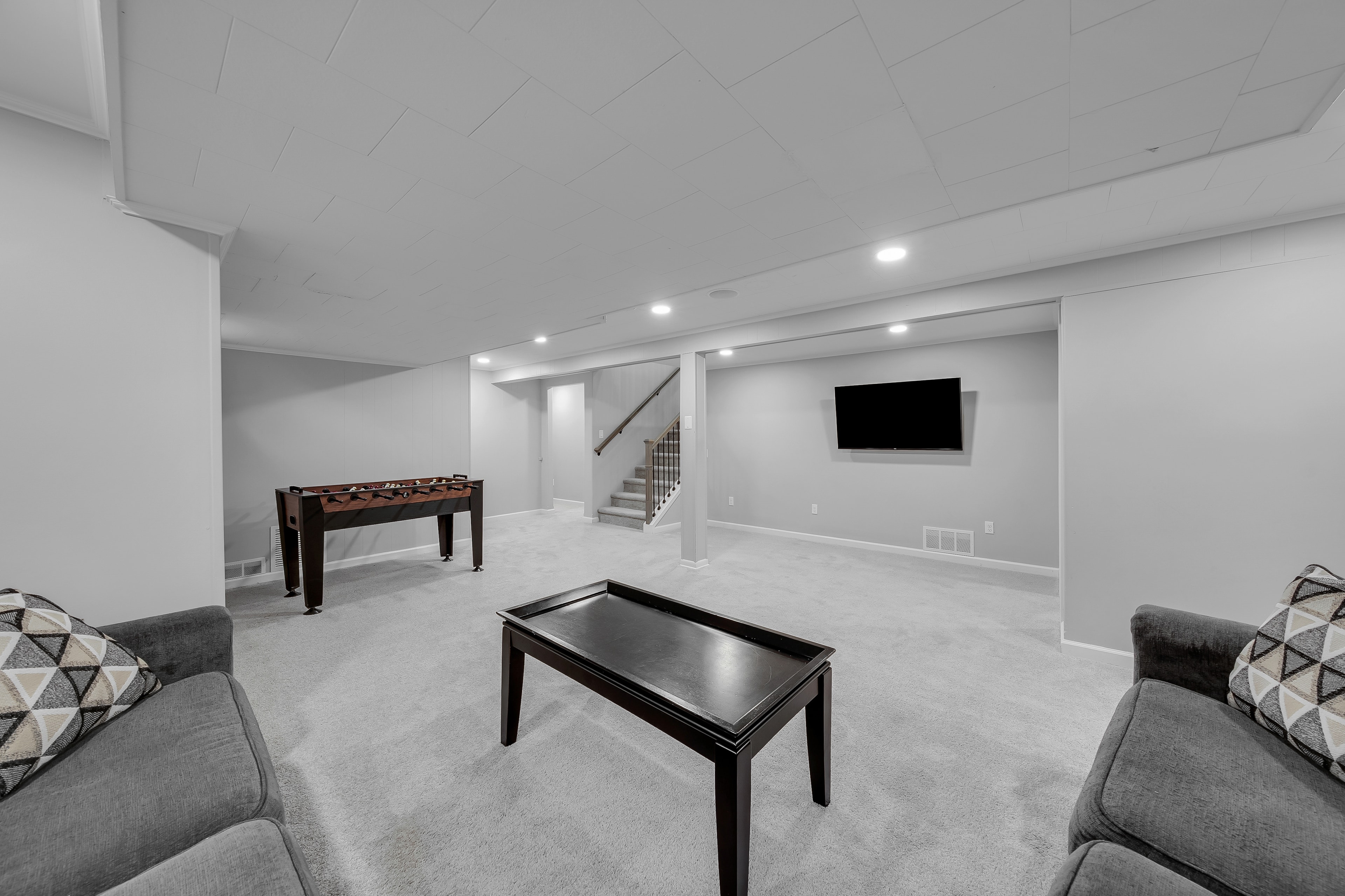 RCVRY HOUSE basement rec room with foosball table, TV, and staircase visible