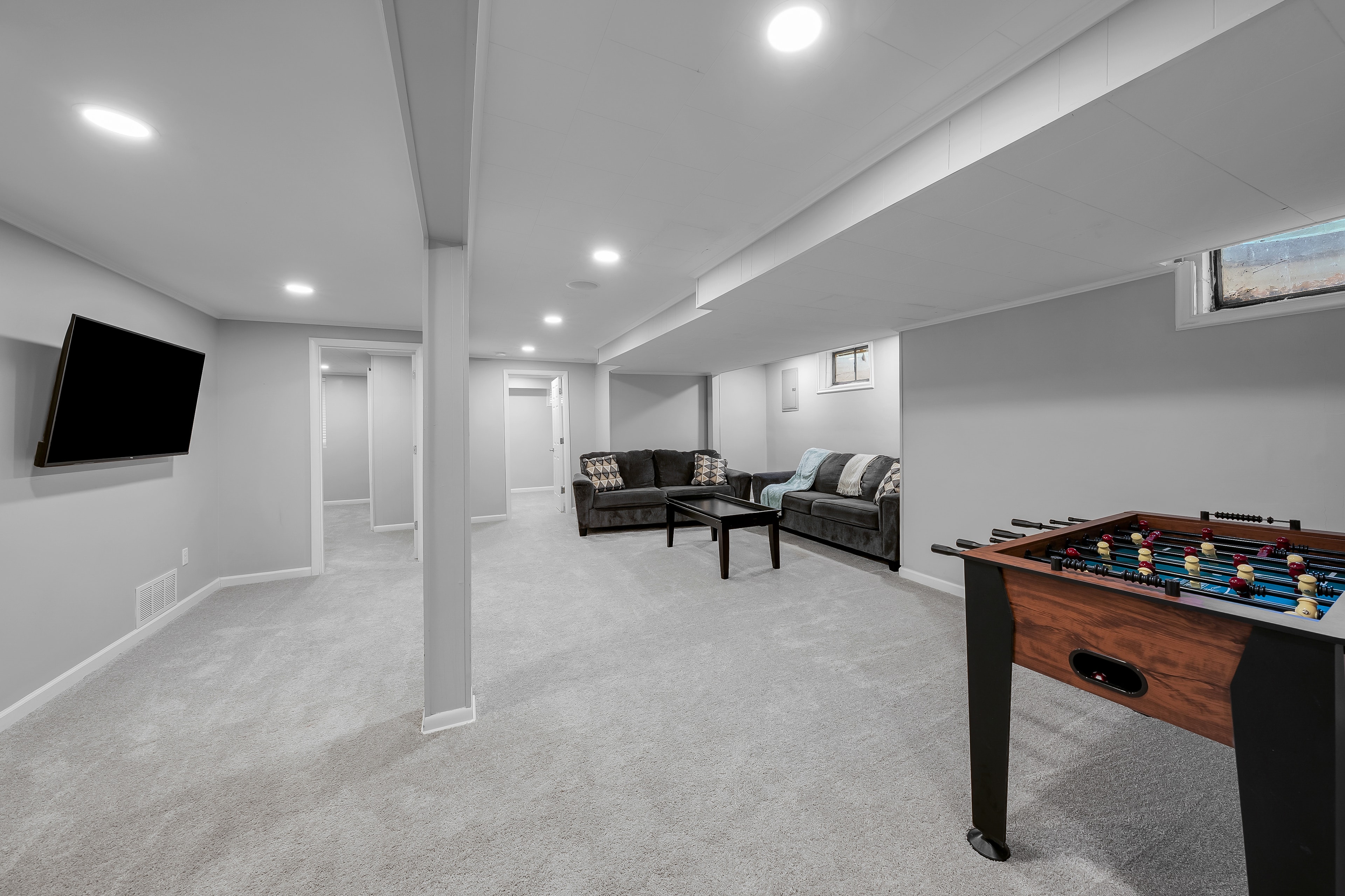 RCVRY HOUSE basement rec room — foosball table, sectional sofas, and Smart TV