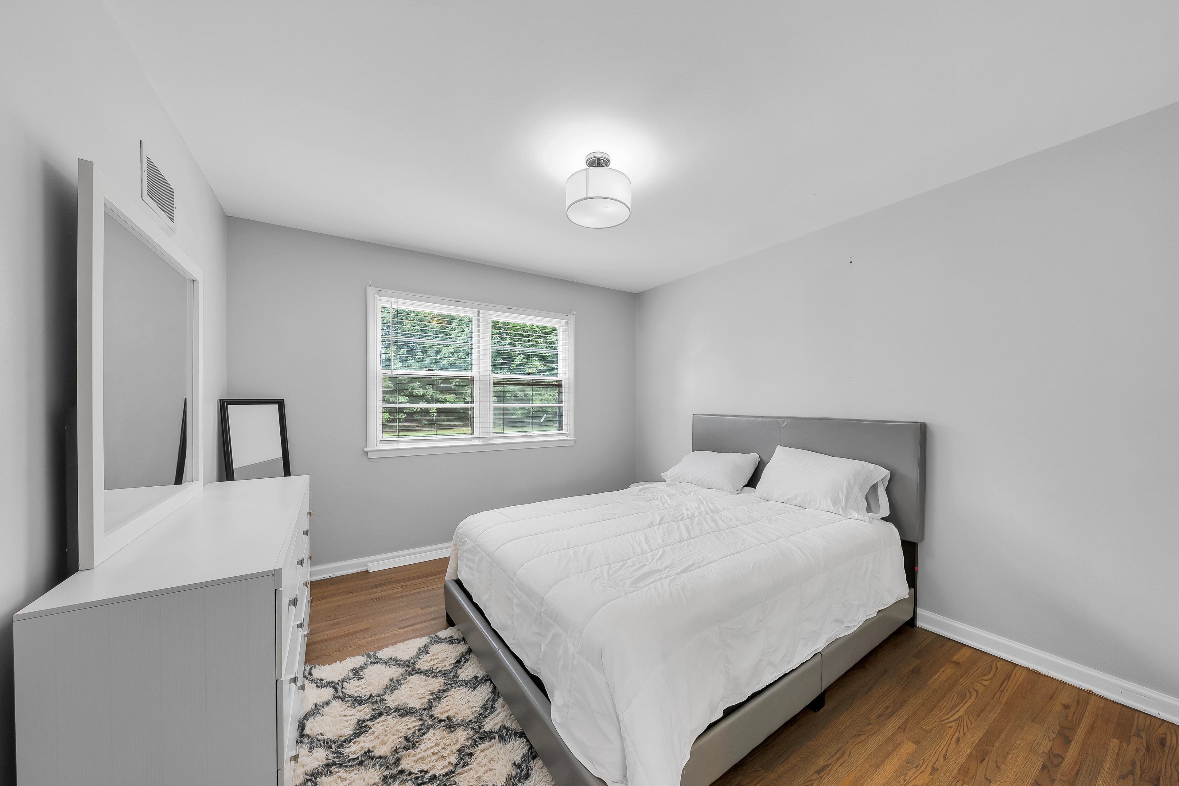 RCVRY HOUSE bedroom with gray bed, pinkish pillows, three framed prints above headboard, and corner mirror